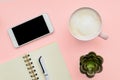 Feminini desk workspace with smartphone, blank notepad, pen, cup of coffee on pink background. flat lay, top view