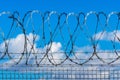 Fence with barbed wire against blue sky with clouds Royalty Free Stock Photo