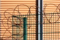 A fence with barbed wire. In the background is a round, orange silo wall.