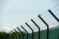 A fence with barbed wire with a bird sitting on it and clear blue sky on the background on the airport Zurich in Switzerland.