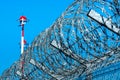 Fence with barbed wire and row of the airport lamp posts with alternate red and white painting against blue sky Royalty Free Stock Photo