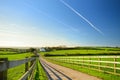 Fence casting shadows on a road leading to small house between scenic Cornish fields under blue sky, Cornwall, England