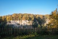 Fence on the edge of the rock wall of the Weilbergsee with autumn forest in the evening light. Royalty Free Stock Photo