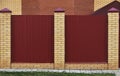 Fence made of bricks and decorative metal. Red fence with yellow elements. High and beautiful fencing