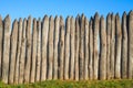 Fence made of sharp wooden stakes against the blue sky. Wooden fence vertical logs pointed against the sky protection against Royalty Free Stock Photo