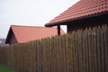 Fence made of sharp wooden stakes, wooden houses with red tiled roof and cloudy sky