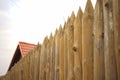 Fence made of sharp wooden stakes and red tiled roof under blue sky