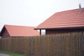 Fence made of sharp wooden stakes. Wooden houses with red tiled roof and sky. Unfocused image