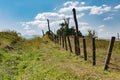 Fence, path, and clouds meeting behind a green hill