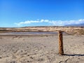 Fence of round wooden posts attached with a rope to delimit the path.Wooden post in desert landscape with lagoon and blue sky.