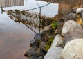 Fence submerged in tidal water with grass and debris by a rocky shore Royalty Free Stock Photo