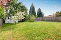 Fenced backyard with grass filled garden and small shed.