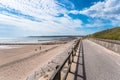 Fenced footpath on a seawall along a sandy beach wuth groynes