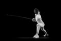 Fencer lunges forward, her blade in motion against black studio background. She is focused and determined, swordswoman