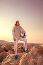 Fencer man standing on top of the rock holding fencing mask and a sword and looking forward seriously Royalty Free Stock Photo