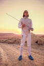 Fencer man wearing white fencing costume holding sword and looking forward