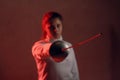 Fencer woman portrait with fencing sword in red light.