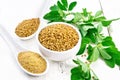 Fenugreek in bowl and two spoons with leaves on light board Royalty Free Stock Photo