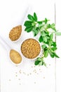 Fenugreek in bowl and two spoons with leaves on light board top Royalty Free Stock Photo