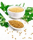 Fenugreek in spoon and bowl with leaves on light wooden board Royalty Free Stock Photo