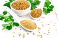 Fenugreek in two spoons and bowl with leaves on light board Royalty Free Stock Photo