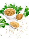 Fenugreek in two spoons and bowl with leaves on white board Royalty Free Stock Photo