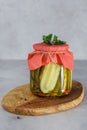 Fermented preserved cucumber in glass jar on wooden stay.