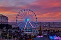 Ferris wheel against sunset pink sky and crowds of people on Christmas market