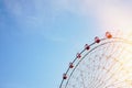 Ferris wheel with bright red booths on background of serene clear blue sky with sunflare as symbol of joy recreation relaxation Royalty Free Stock Photo