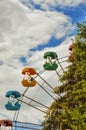 Ferris wheel in the city Park. green tree, spruce and blue sky with white clouds.