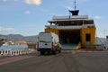 A ferry is moored in the port and a transport vehicle pulls into it on an open ramp. Commercial and cargo transportation