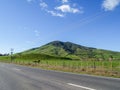 Fertile green grassland hill from road under blue sky