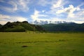 Fertile valley with pasture on the hill against the backdrop of snowy mountain peaks