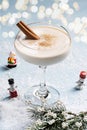 Festive alcoholic cocktail eggnog in a beautiful glass on a blue background, strewn with snow