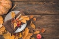 Festive autumn background with a plate, cutlery, napkin, pumpkin and autumn leaves on a wooden background.