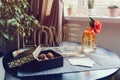 Festive box with chocolate macaroons cakes, rose flower in vase, postcard and wire word Love on the black table near window. Cozy