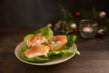 Festive canapes from baguette bread with salmon and cream cheese on green lettuce on a dark rustic wooden table with Christmas