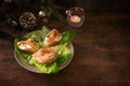 Festive canapes from baguette bread with salmon and cream cheese on a plate with green lettuce, dark rustic wooden table with