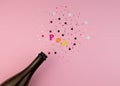 Festive Champagne bottle with colorful glittering stars splashes on pink background. Minimal party concept Royalty Free Stock Photo