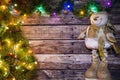 Festive Christmas background of dark old wooden boards, fir-tree, snowman and luminous garland with colored lights and Christmas b Royalty Free Stock Photo