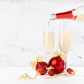 Festive christmas background with stream of pouring fizz champagne from bottle to two glasses, bright christmas decorations - red.