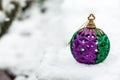 Festive Christmas ball colored in green and purple in the winter day on a white snow with copy space on the left