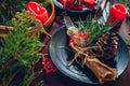 Festive Christmas dinner table setting for two decorated with fir branches, red candles, cones, ornaments. Royalty Free Stock Photo