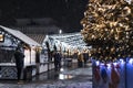 Festive Christmas and New Year's fair square in the city at night, falling snow, New Year tree and houses with garlands. Royalty Free Stock Photo