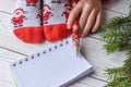 A Christmas photo with feminine feet in bright red socks, a fir twig, a note book and a pencil on a white wooden floor