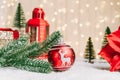 Festive composition with fir tree branch, red bauble ball decor, small Christmas trees, lantern on the snow against a Royalty Free Stock Photo
