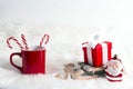 Festive composition with red mug, toy sled with gift box and little santa over fur background