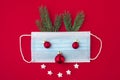 Festive coronavirus christmas concept made from face mask, fir tree and decorations on red background. flat lay Royalty Free Stock Photo
