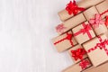 Festive craft paper gifts with red bows closeup on soft white wood board, top view, border. Royalty Free Stock Photo