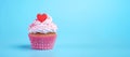 festive cupcake with cream, decorated with heart and sprinkles, on blue background, copy space